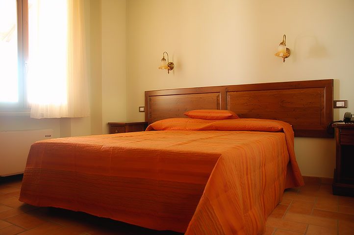 Camera matrimoniale con copriletto arancio e testiera in legno