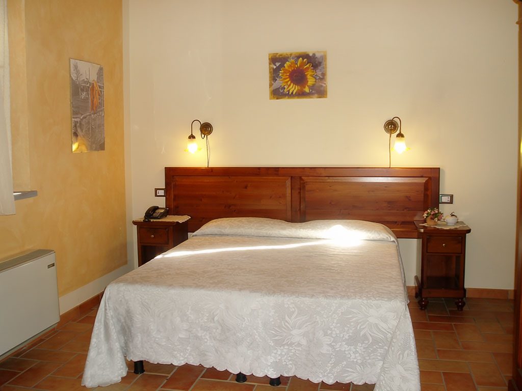 Camera matrimoniale con copriletto bianco e comodini in legno
